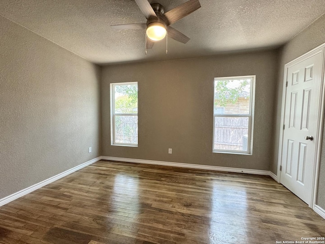 interior space with a ceiling fan, a textured ceiling, wood finished floors, baseboards, and a textured wall