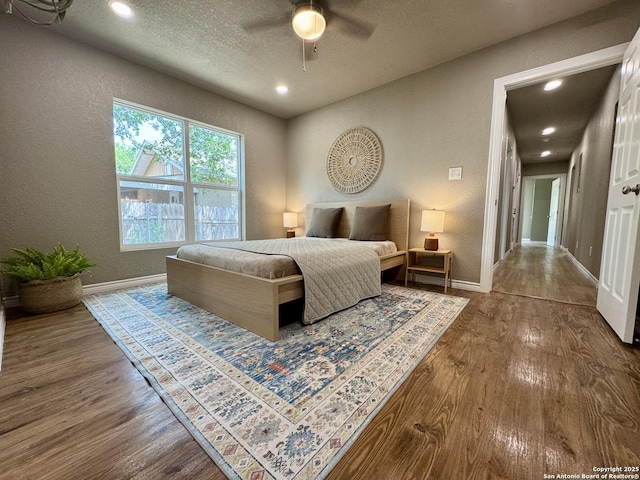 bedroom with baseboards, recessed lighting, a textured wall, and dark wood-style floors