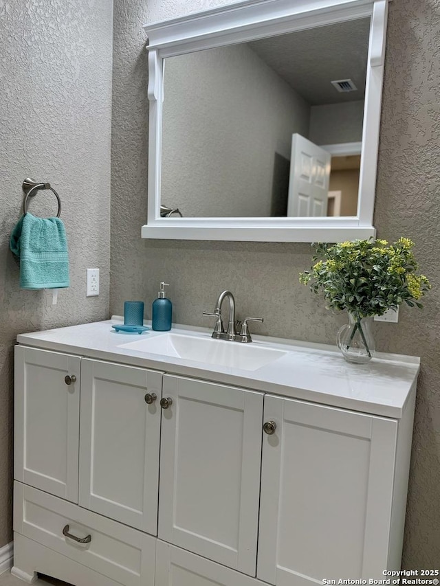 bathroom with a textured wall, visible vents, and vanity