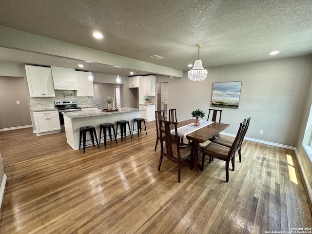 dining space with baseboards, a textured ceiling, a chandelier, and wood finished floors