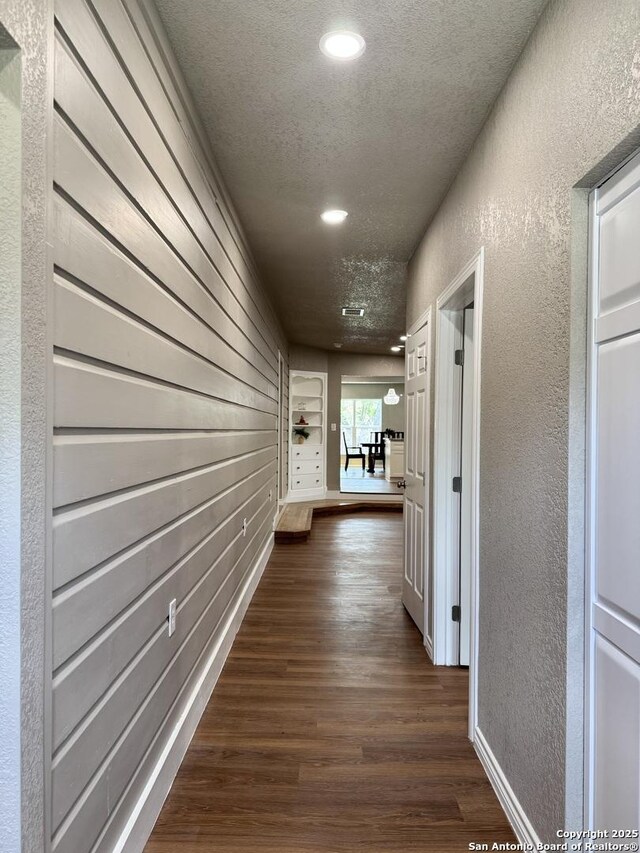 hallway with recessed lighting, a textured wall, dark wood-style floors, and a textured ceiling