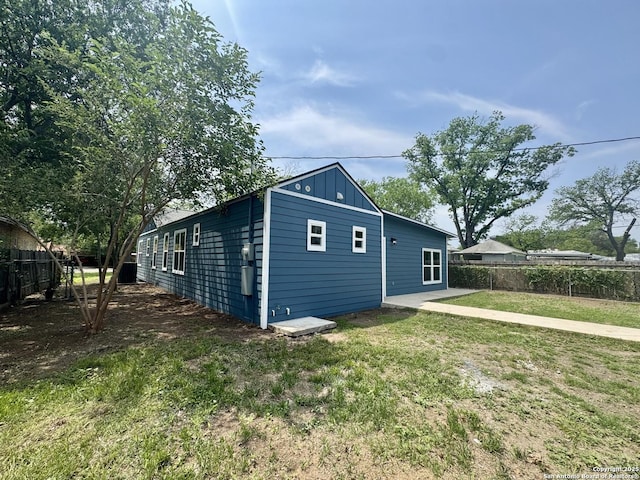 view of side of property with a lawn, board and batten siding, and fence