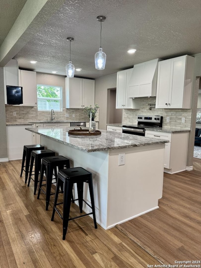 kitchen with stainless steel electric range, wood finished floors, backsplash, a spacious island, and custom exhaust hood