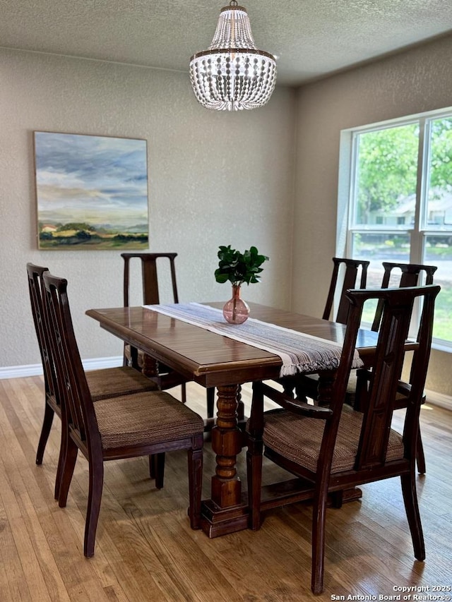 dining area with a wealth of natural light, a textured wall, light wood finished floors, and a chandelier