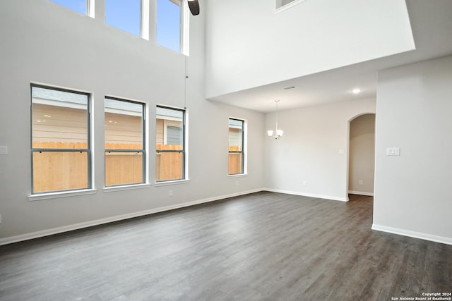 unfurnished living room featuring dark wood-type flooring, arched walkways, baseboards, and a wealth of natural light