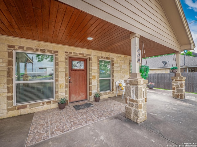 view of exterior entry featuring a porch, fence, and stone siding