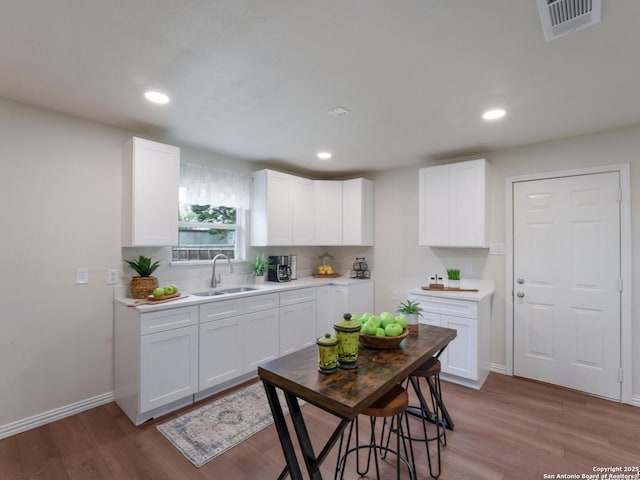 kitchen with visible vents, wood finished floors, a sink, light countertops, and white cabinetry