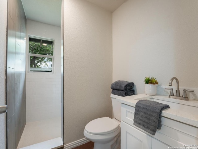 bathroom featuring vanity, a textured wall, a tile shower, and toilet