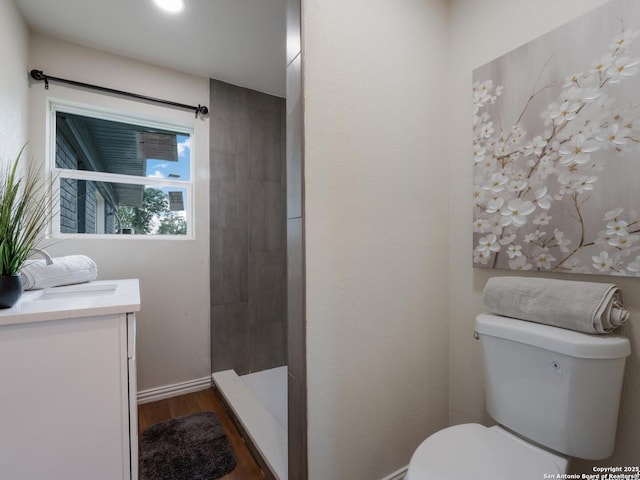 bathroom featuring vanity, wood finished floors, a tile shower, and toilet