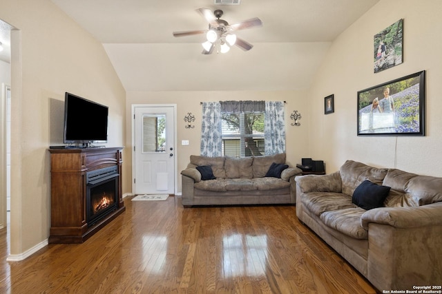 113 E Dawn Dr, Johnson City, TX 78636 - living room featuring a ceiling fan, visible vents, vaulted ceiling, dark wood-style floors, and a warm lit fireplace