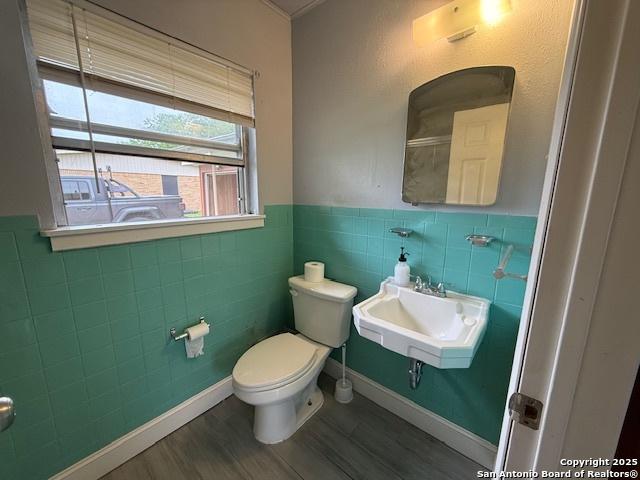 4519 Creekmoor, San Antonio, TX 78220 - bathroom featuring a sink, wood finished floors, toilet, tile walls, and a wainscoted wall
