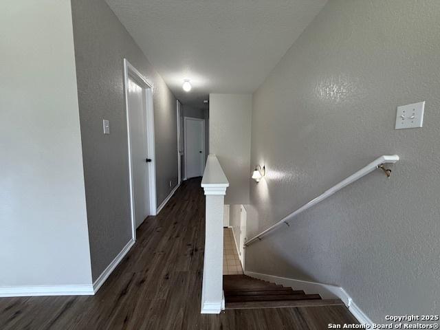 corridor featuring baseboards, a textured wall, and wood finished floors