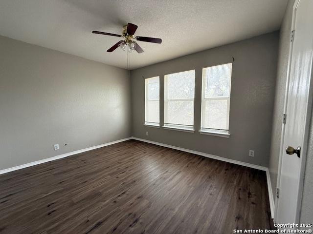 empty room featuring baseboards, ceiling fan, and dark wood-type flooring