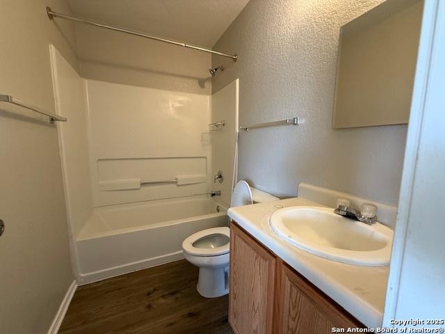 bathroom with a textured wall, vanity, shower / bathtub combination, toilet, and wood finished floors