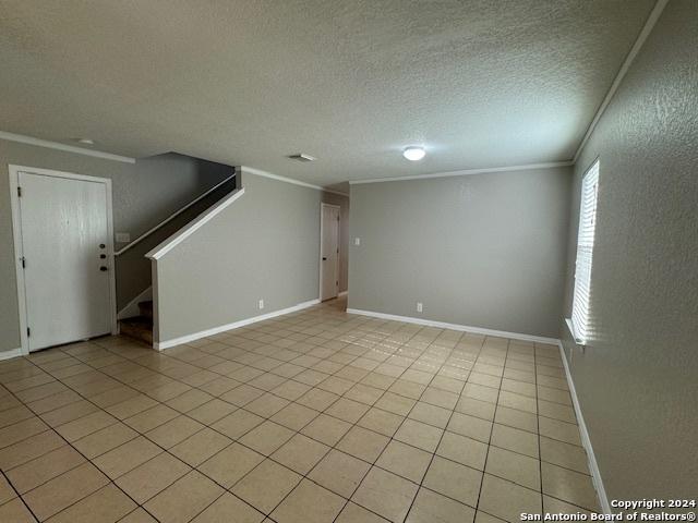 spare room featuring baseboards, ornamental molding, light tile patterned floors, and stairway