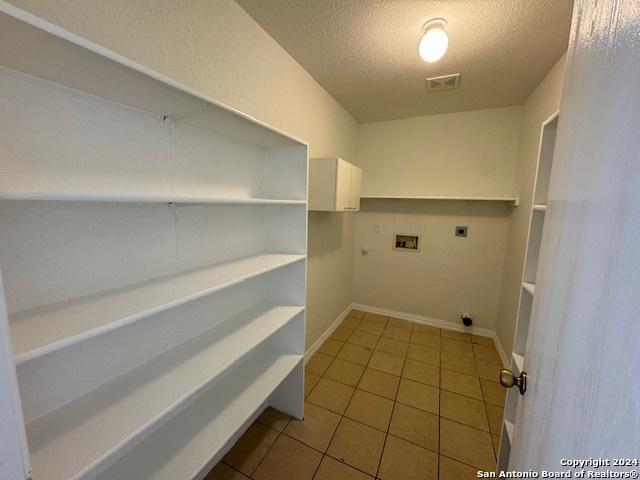 laundry area with laundry area, hookup for a washing machine, a textured ceiling, tile patterned floors, and electric dryer hookup
