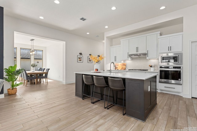 140 Cordova, Boerne, TX 78006 - kitchen featuring stainless steel appliances, backsplash, light countertops, light wood finished floors, and an island with sink