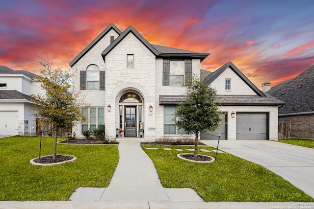 french provincial home featuring a yard, concrete driveway, stone siding, and a garage