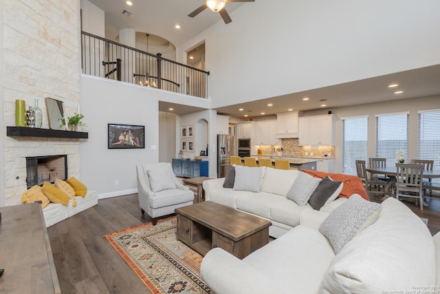 living room featuring a stone fireplace, a ceiling fan, dark wood-style floors, and recessed lighting