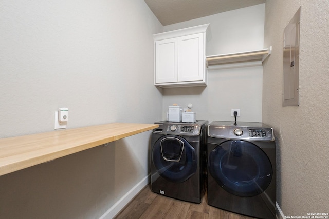 clothes washing area with electric panel, washing machine and dryer, cabinet space, wood finished floors, and baseboards