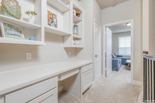 unfurnished office with baseboards, built in desk, and light carpet