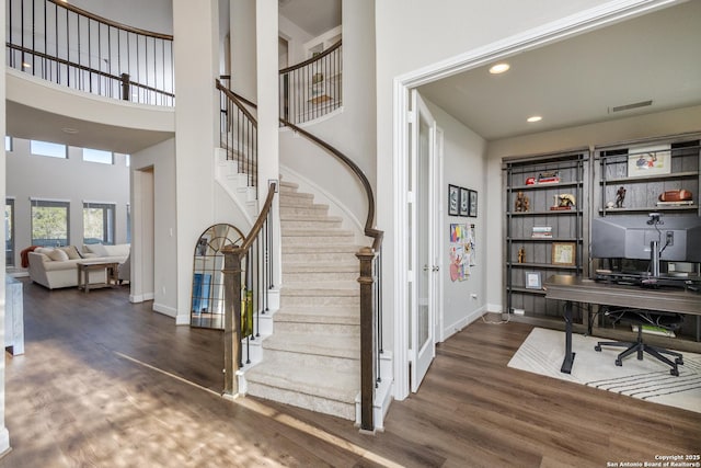 staircase with baseboards, a towering ceiling, wood finished floors, and visible vents