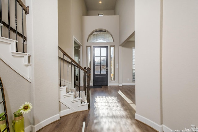 entryway with baseboards, wood finished floors, stairway, and a towering ceiling