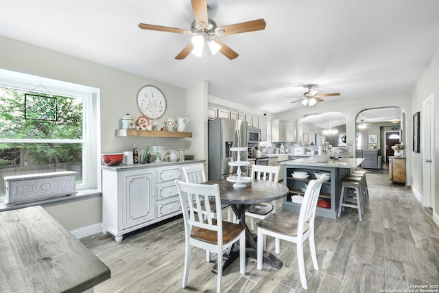 dining area with a ceiling fan, arched walkways, baseboards, and light wood-style floors