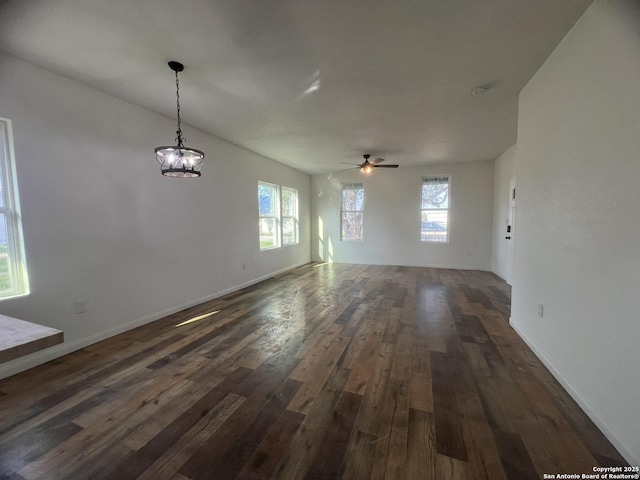 unfurnished dining area featuring dark wood-style flooring, baseboards, a wealth of natural light, and ceiling fan with notable chandelier