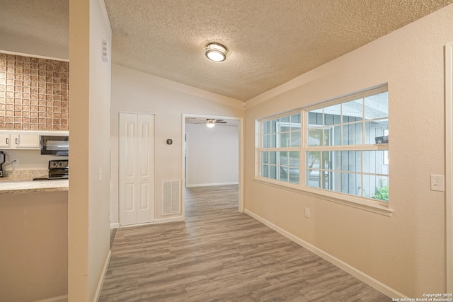 hall with wood finished floors, lofted ceiling, a textured ceiling, and visible vents