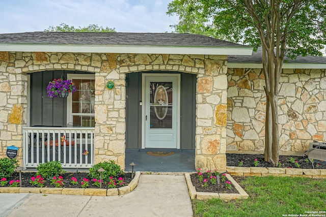 doorway to property with a porch, roof with shingles, and stone siding