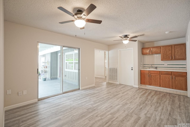 unfurnished living room featuring light wood finished floors, a textured ceiling, a ceiling fan, baseboards, and visible vents