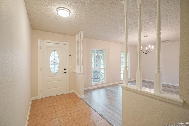 entrance foyer featuring light tile patterned flooring, a textured ceiling, a notable chandelier, and baseboards