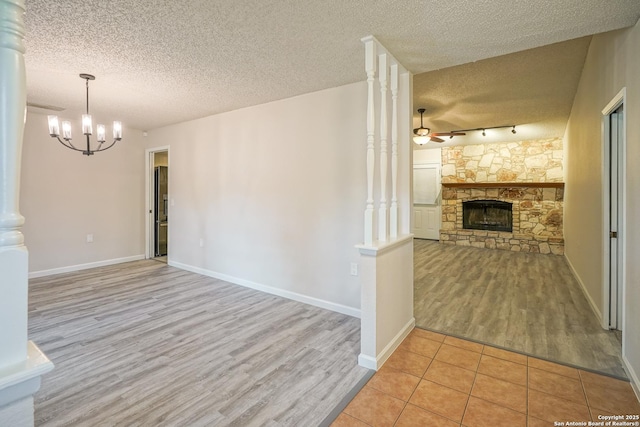 unfurnished living room featuring a textured ceiling, a stone fireplace, wood finished floors, and ceiling fan with notable chandelier