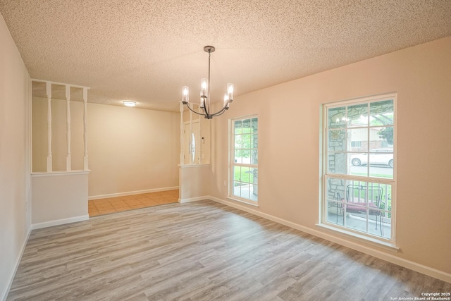 spare room featuring a textured ceiling, an inviting chandelier, a wealth of natural light, and wood finished floors
