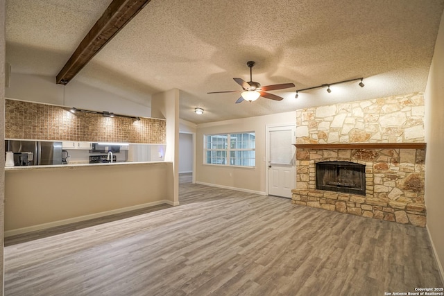 unfurnished living room with ceiling fan, a textured ceiling, a fireplace, wood finished floors, and lofted ceiling with beams