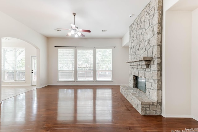 unfurnished living room featuring a ceiling fan, baseboards, a stone fireplace, and wood finished floors