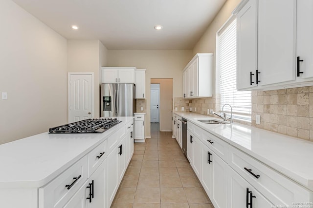 kitchen featuring appliances with stainless steel finishes, a sink, light countertops, backsplash, and a kitchen island