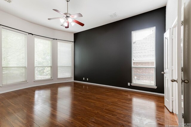 empty room with plenty of natural light, a ceiling fan, wood finished floors, and visible vents