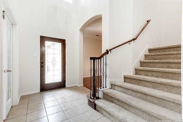foyer featuring baseboards, arched walkways, light tile patterned floors, and stairway