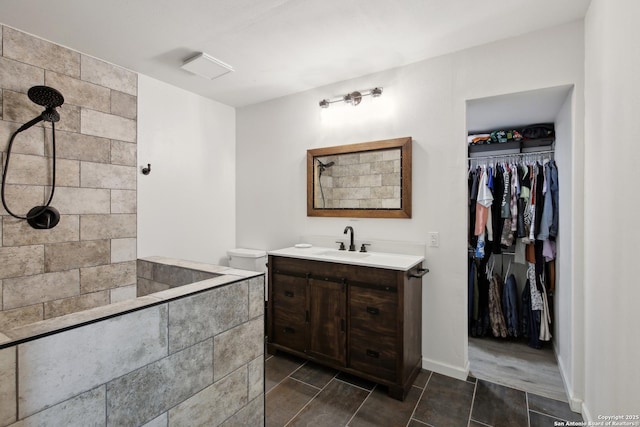 full bath with vanity, baseboards, a tile shower, and a walk in closet