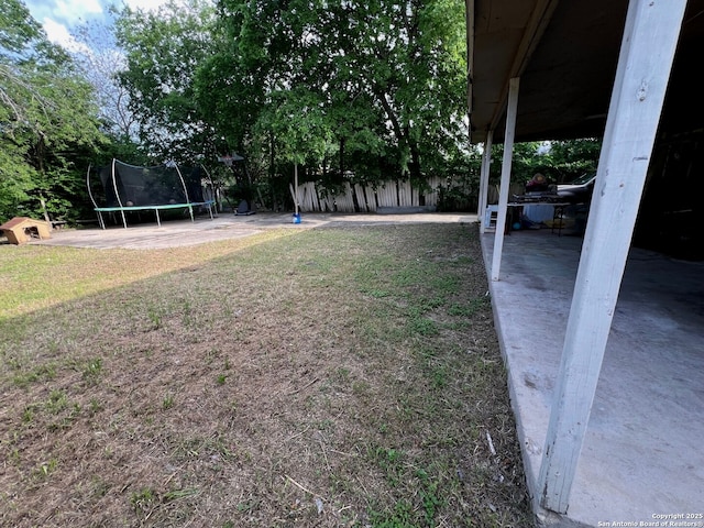 view of yard featuring a trampoline, a patio area, and fence