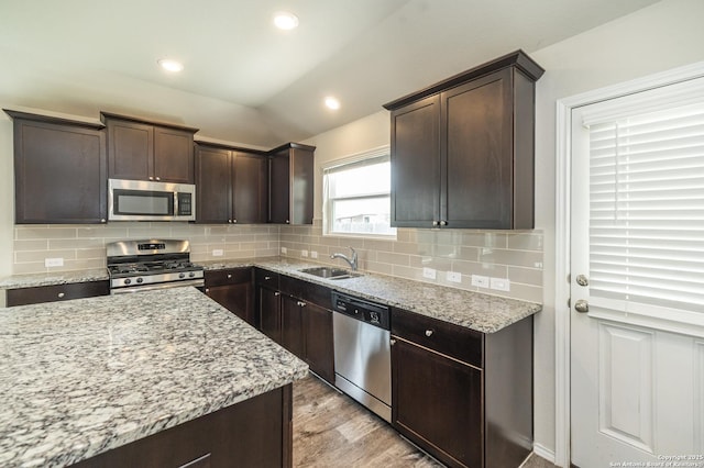 kitchen with light stone countertops, dark brown cabinets, light wood-style floors, a sink, and stainless steel appliances