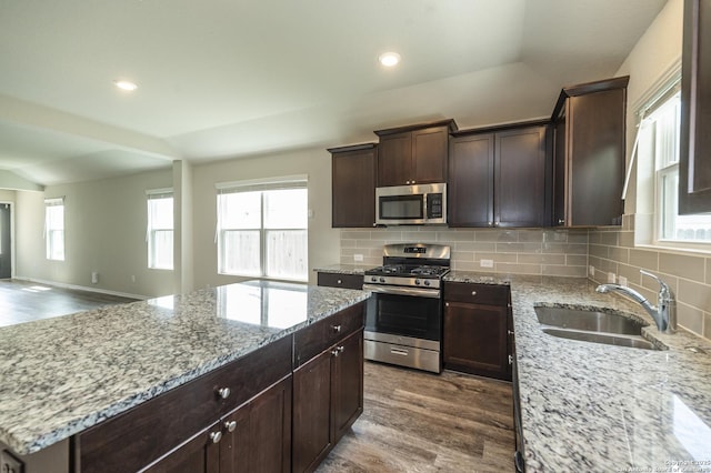 kitchen with light stone countertops, vaulted ceiling, wood finished floors, a sink, and stainless steel appliances