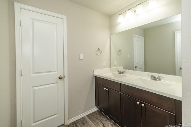 bathroom featuring a sink, baseboards, double vanity, and wood finished floors