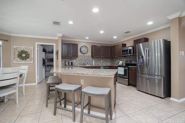kitchen featuring visible vents, dark brown cabinets, a kitchen breakfast bar, light tile patterned floors, and stainless steel appliances