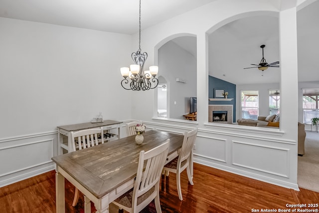 dining area with arched walkways, a fireplace, wainscoting, and wood finished floors