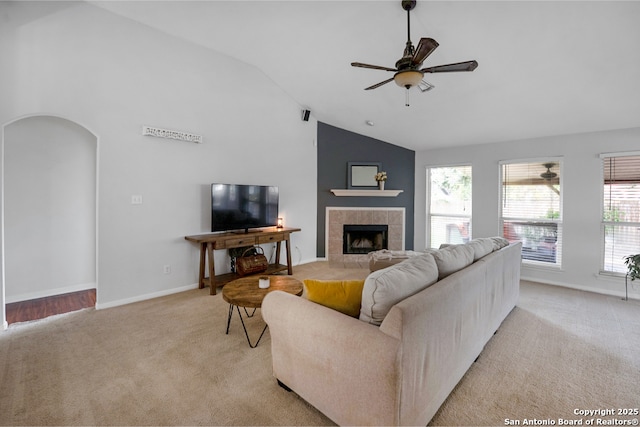 living room with a healthy amount of sunlight, a ceiling fan, light colored carpet, a tiled fireplace, and baseboards