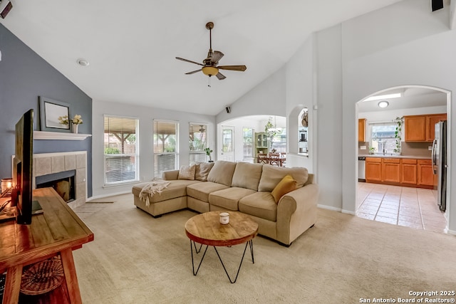 living area featuring ceiling fan, light colored carpet, arched walkways, high vaulted ceiling, and a tile fireplace