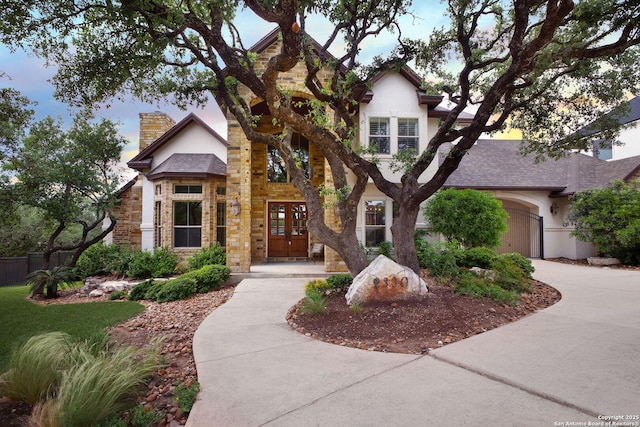 view of front of property with driveway, a chimney, stone siding, and stucco siding